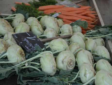 Nahaufnahme von Kohlrabi und Karotten auf einem Marktstand.