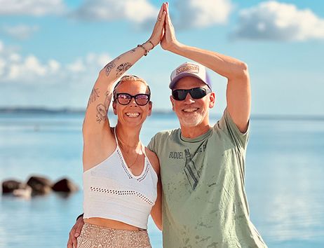 Ein Mann und eine Frau stehen am Strand und machen eine Yogaübung vor dem Meer.