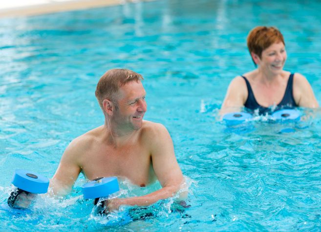 Zwei Personen machen Wassergymnastik mit Hanteln im Pool.