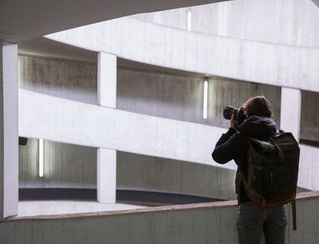 Ein Fotograf mit Rucksack fotografiert in einem spiralförmigen Parkhaus.