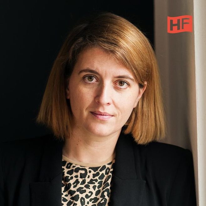 Porträt einer Frau mit schulterlangem Haar und einem schwarzen Blazer vor einem dunklen Hintergrund.