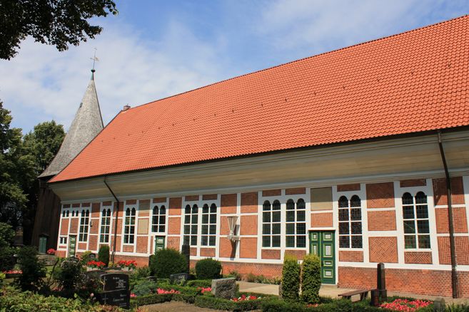 Außenansicht der Dreieinigkeitskirche in Allermöhe mit rotem Ziegeldach und Fachwerkfassade.