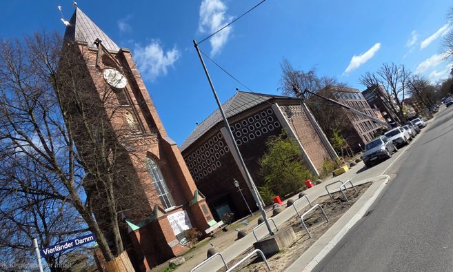 Kirche mit Turm und Uhr an einer Straße mit parkenden Autos.
