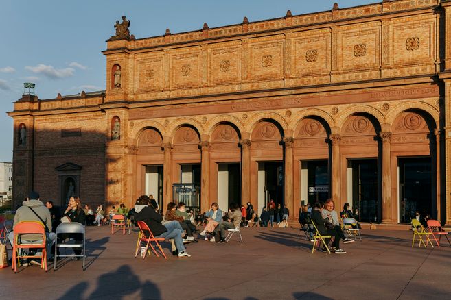 Menschen sitzen auf bunten Stühlen vor der Fassade der Hamburger Kunsthalle im warmen Abendlicht.