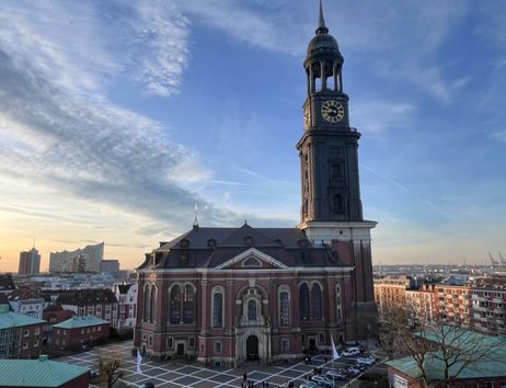 Die Kirche St. Michaelis in Hamburg bei Sonnenuntergang mit der Elbphilharmonie im Hintergrund.