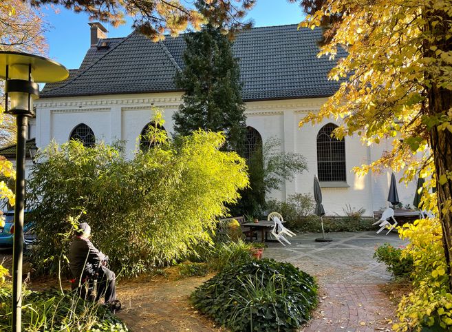 Ein ruhiger Garten mit Herbstlaub vor einer weißen Kirche mit gotischen Fenstern.