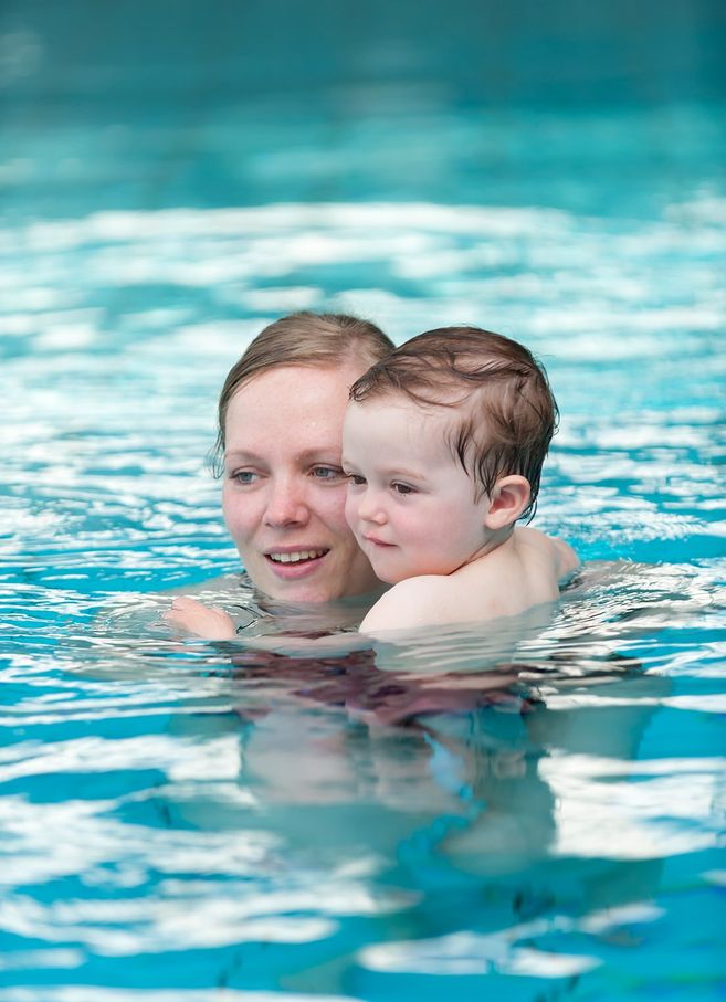 Eine Frau hält ein Kleinkind im Wasser eines Schwimmbeckens.