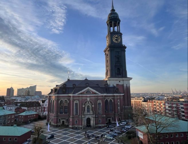 Die Kirche St. Michaelis in Hamburg bei Sonnenuntergang, mit der Elbphilharmonie im Hintergrund.