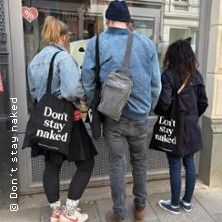 Drei Personen stehen vor einem Schaufenster in Hamburg. Zwei von ihnen tragen Taschen mit der Aufschrift 'Don't stay naked'.
