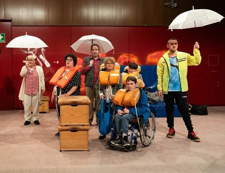 Eine Gruppe von Menschen mit Rettungswesten und Regenschirmen in einem Raum mit roter Wand.