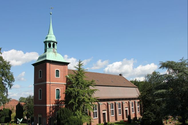 Kirche St. Pankratius in Ochsenwerder mit rotem Backstein und grünem Turm unter blauem Himmel.
