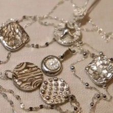 Mehrere silberne Schmuckanhänger mit unterschiedlichen Stempeln und Texturen auf einer Kette, passend zum Titel „Art Clay Silber: Stempel & Texturkurs - Creative Silver Session“.