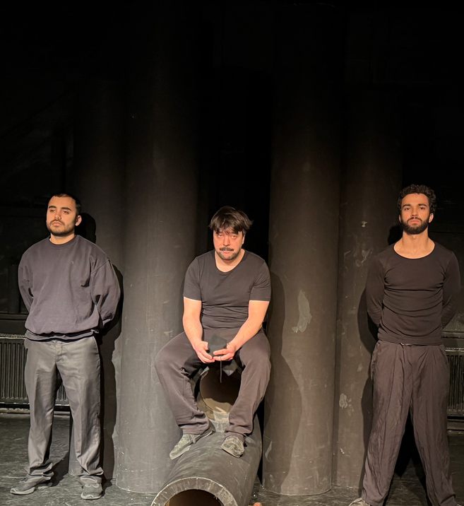 Es sind Drei Männer abgebildet, der in der Mitte sitzt auf einem Rohr, während die anderen zwei zu seiner Seite Wache stehen. von links nach rechts: Quentin Barich als Wache 1, Emrah Demir als Sipan und Marlon Mähnert als Wache 2