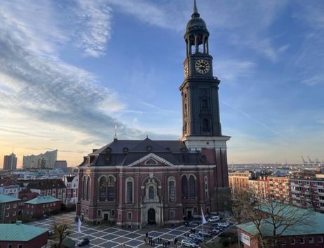 Die Kirche St. Michaelis in Hamburg mit ihrem markanten Turm und der Elbphilharmonie im Hintergrund bei Sonnenuntergang.