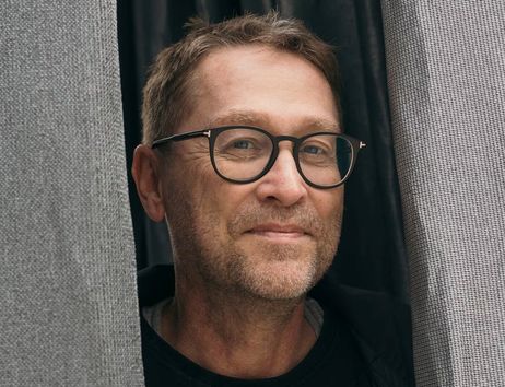 Ein Mann mit Brille schaut zwischen zwei Vorhängen hervor.