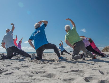 Eine Gruppe von Menschen macht Gymnastikübungen am Strand unter blauem Himmel.