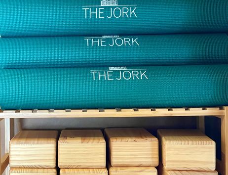 Gestapelte grüne Yogamatten mit der Aufschrift 'THE JORK' und darunter Holzblöcke in einem Regal.
