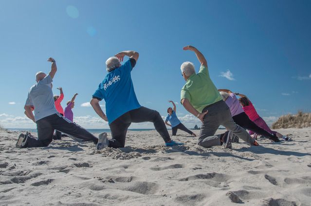 Eine Gruppe von Menschen macht Gymnastikübungen am Strand unter blauem Himmel.