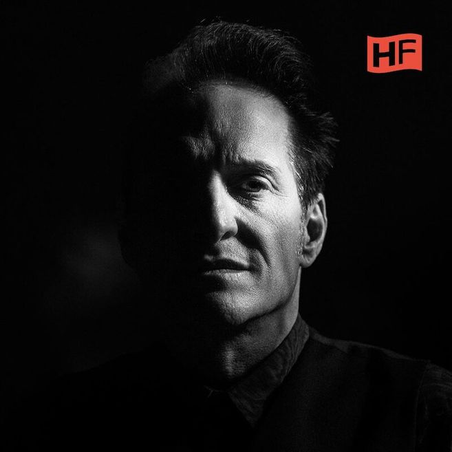 Schwarz-weiß Porträt eines Mannes mit Schatten auf der linken Gesichtshälfte und einem HF-Logo oben rechts.