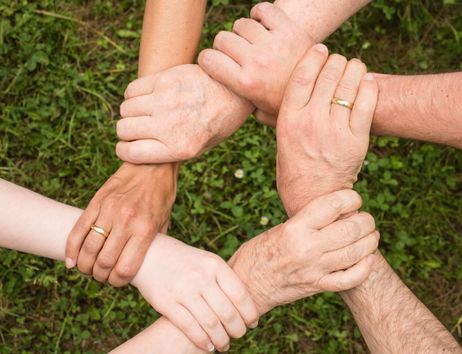 Sechs Hände, die sich im Kreis am Handgelenk umfassen