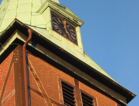 Nahaufnahme eines Kirchturms mit Uhr und Fachwerk.