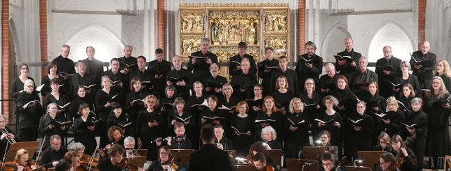Ein Chor singt in einer Kirche vor einem kunstvollen Altar.
