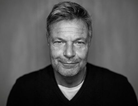 Schwarz-weiß Porträt eines lächelnden Mannes mit Bart und kurzen Haaren.
