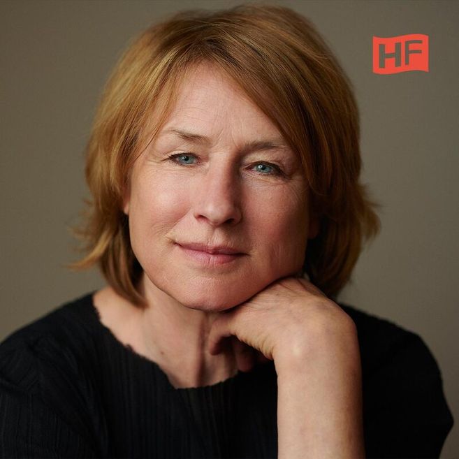 Porträt einer Frau mit kurzen, blonden Haaren, die ihr Kinn auf ihre Hand stützt. Im Hintergrund ist ein Logo mit den Buchstaben 'HF' zu sehen.