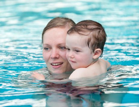 Eine Frau hält ein Kleinkind im Wasser eines Schwimmbeckens.