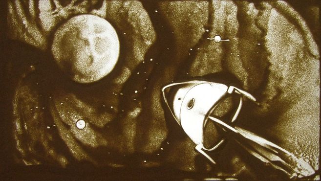 Sandkunstwerk einer Rakete im Weltraum mit Mond und Saturn im Hintergrund.