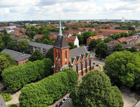Luftaufnahme einer Kirche inmitten einer Wohngegend mit vielen Bäumen.