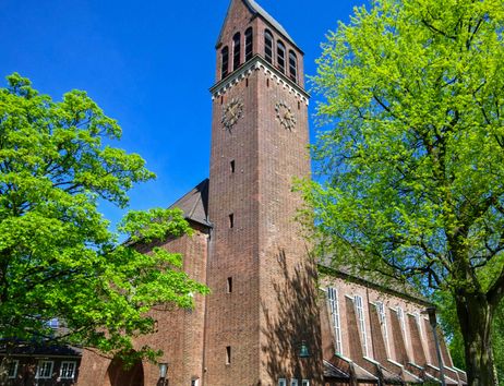 Backsteinkirche mit Turm und grünen Bäumen im Vordergrund.