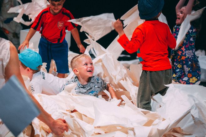 Kinder spielen fröhlich in einem Raum voller zerknülltem weißem Papier und haben sichtlich Spaß dabei.