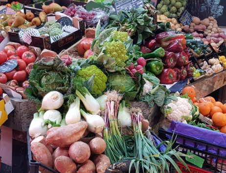 Ein Marktstand mit frischem Obst und Gemüse, darunter Tomaten, Paprika, Fenchel, Blumenkohl und Süßkartoffeln.