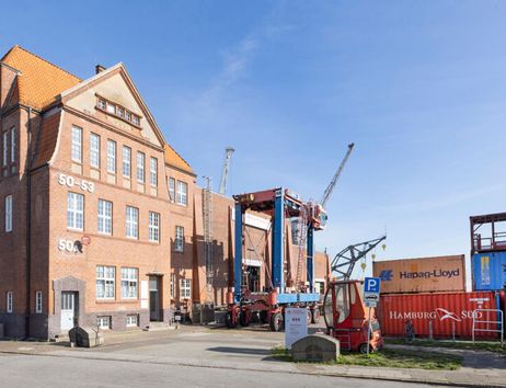 Backsteingebäude mit Containern und Kran im Hafenbereich.