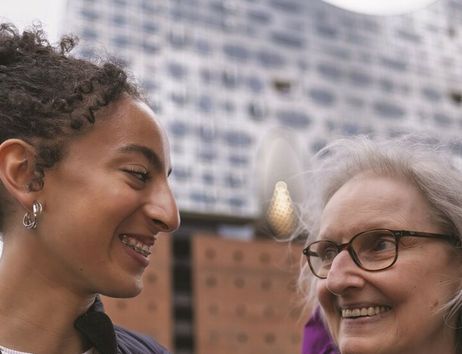 Zwei Frauen lächeln sich vor der Elbphilharmonie in Hamburg an.