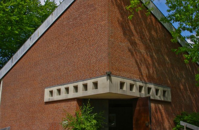 Backsteingebäude mit geometrischen Mustern und offenem Eingang, umgeben von Bäumen.
