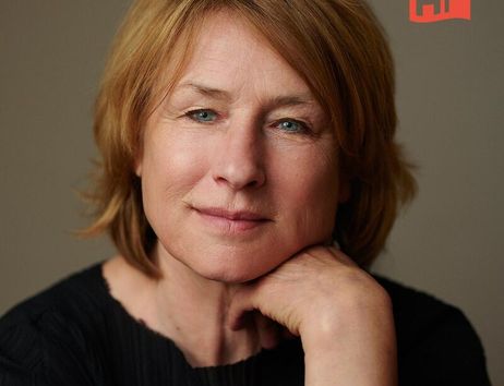 Porträt einer Frau mit kurzen, blonden Haaren, die ihr Kinn auf ihre Hand stützt. Im Hintergrund ist ein Logo mit den Buchstaben 'HF' zu sehen.
