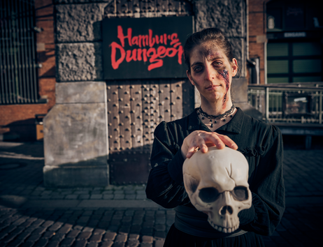 Geschminkte Schauspielerin steht vor dem Hamburg Dungeon Logo