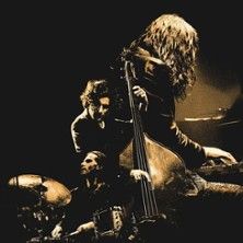 Drei Musiker spielen Jazz auf einer Bühne, einer am Schlagzeug, einer am Kontrabass und einer am Keyboard.