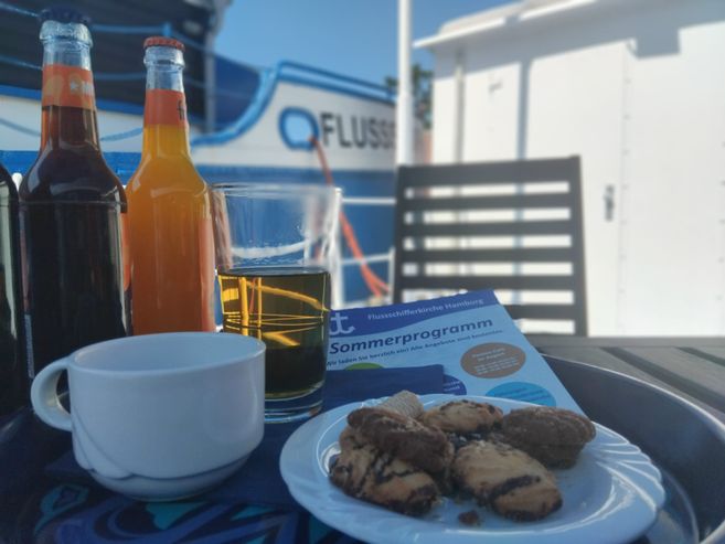 Ein Kaffee- und Kuchengedeck mit Softdrinks auf dem sommerlichen Ponton der Flussschifferkirche Hamburg.