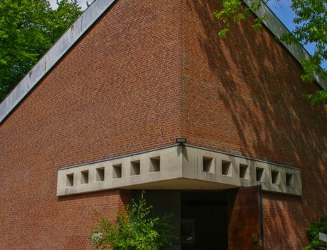 Backsteingebäude mit geometrischen Mustern und offenem Eingang, umgeben von Bäumen.