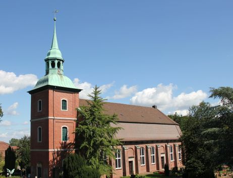 Kirche St. Pankratius in Ochsenwerder mit rotem Backstein und grünem Turm vor blauem Himmel.