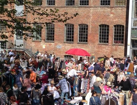Menschenmenge auf einem Flohmarkt vor einem Backsteingebäude.