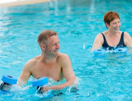 Zwei Personen machen Wassergymnastik mit Hanteln im Pool.