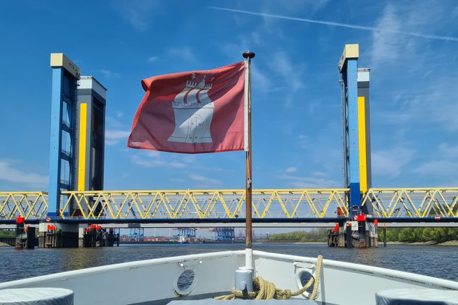 Am Bug eines Schiffs flattert eine Hamburg-Fahne, während das Schiff auf die Kattwykbrücken zusteuert.