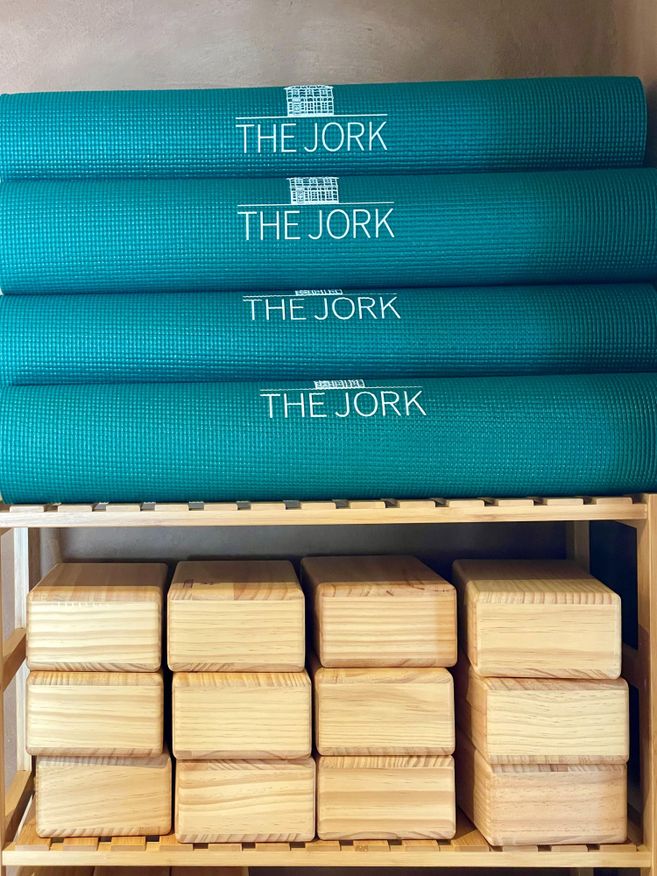 Gestapelte grüne Yogamatten mit der Aufschrift 'THE JORK' und darunter Holzblöcke in einem Regal.