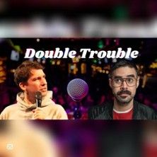 Zwei Männer mit Mikrofonen vor unscharfem Hintergrund und dem Text 'Double Trouble'.
