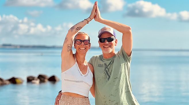 Ein Mann und eine Frau stehen am Strand und machen eine Yogaübung vor dem Meer.