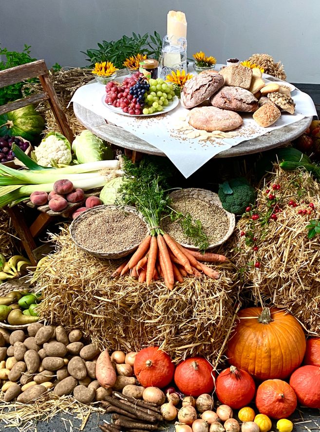 Ein Erntedankaltar mit Brot, Trauben, Gemüse und Getreide auf Strohballen dekoriert.